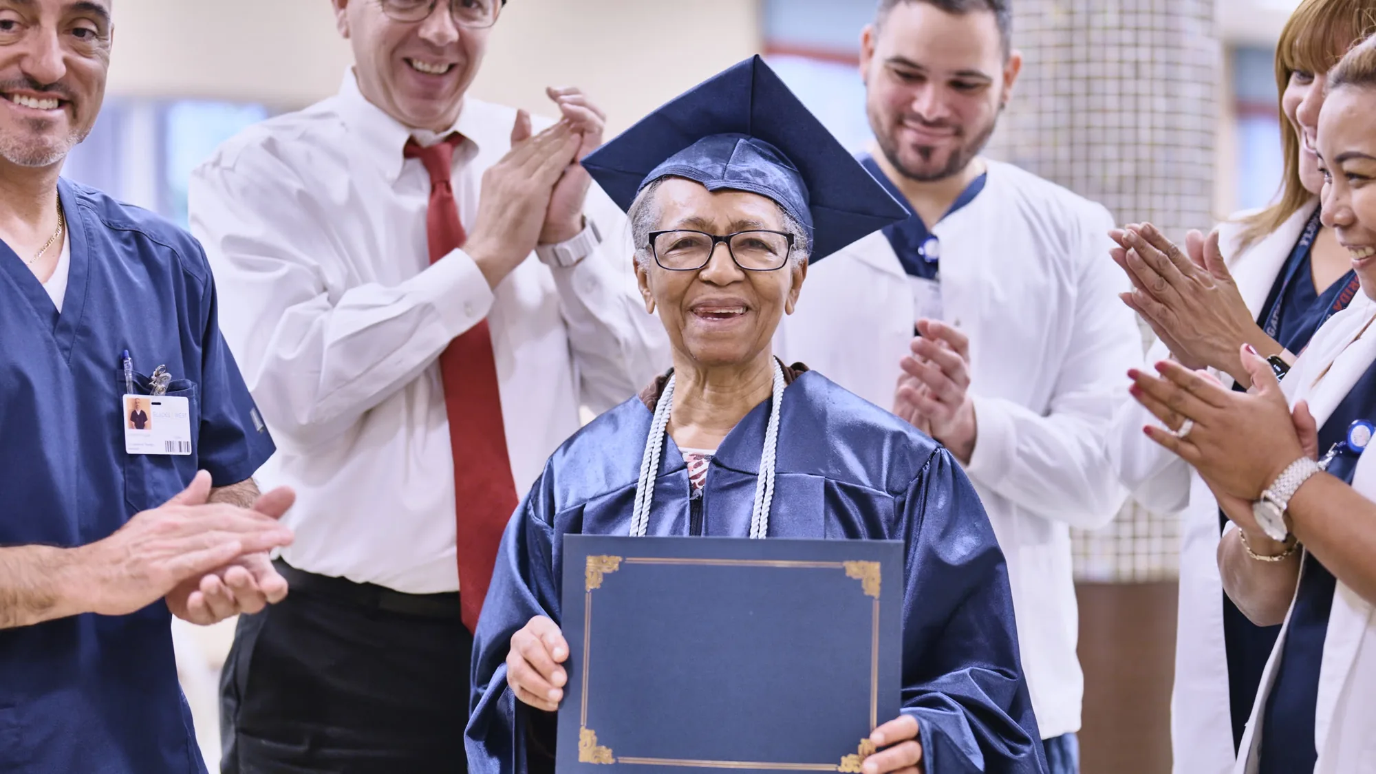 Glades West — staff applauding a resident in a graduation cap and gown