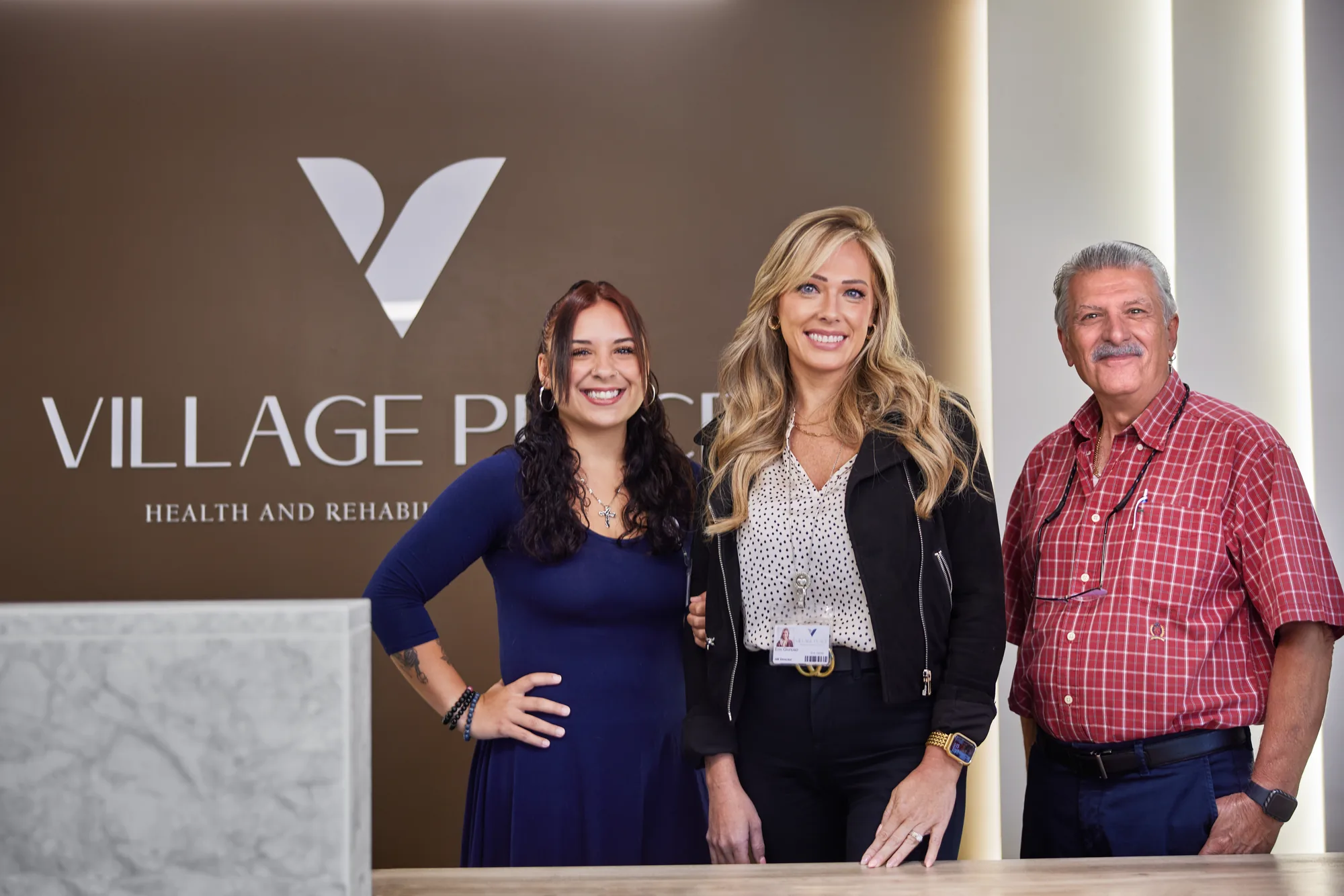 Village Place — three staff members in front of the lobby sign